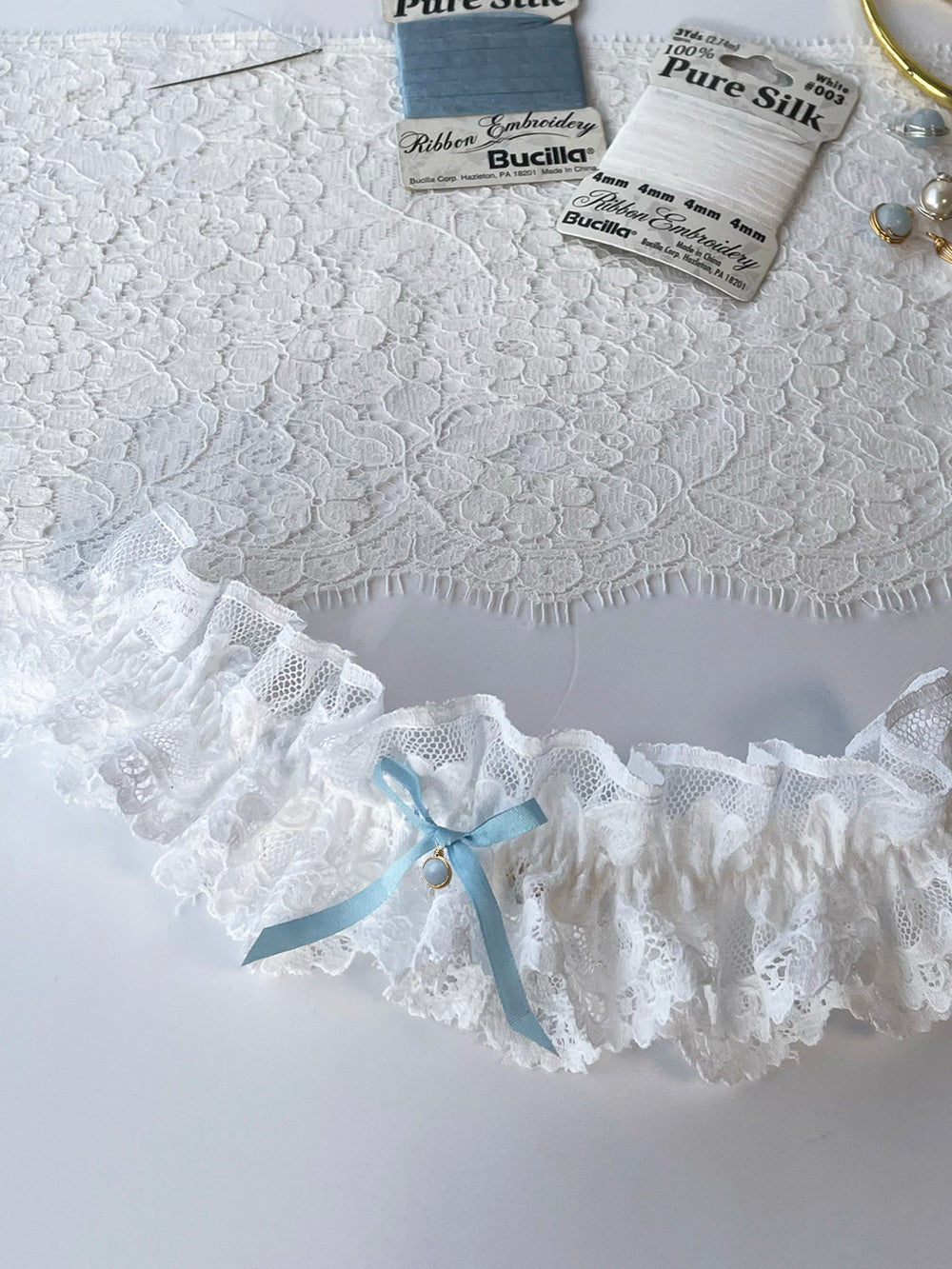Clara white lace garter close-up with blue satin bow and lace detail - handmade bridal lingerie Brighton