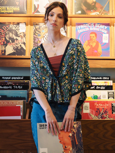 Woman in a Rachel Meadow Liberty Silk Bed Jacket standing in front of a record player with vinyl records on a shelf.