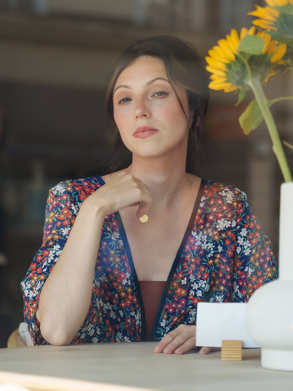 Woman in a Sea Blossom Navy Silk Bed Jacket sitting at a table with a sunflower in the background