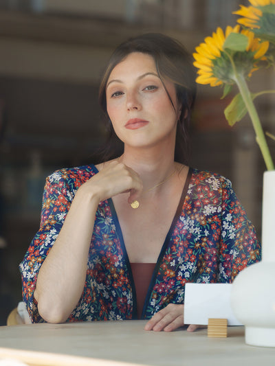 Woman in a Sea Blossom Navy Silk Bed Jacket sitting at a table with a sunflower in the background