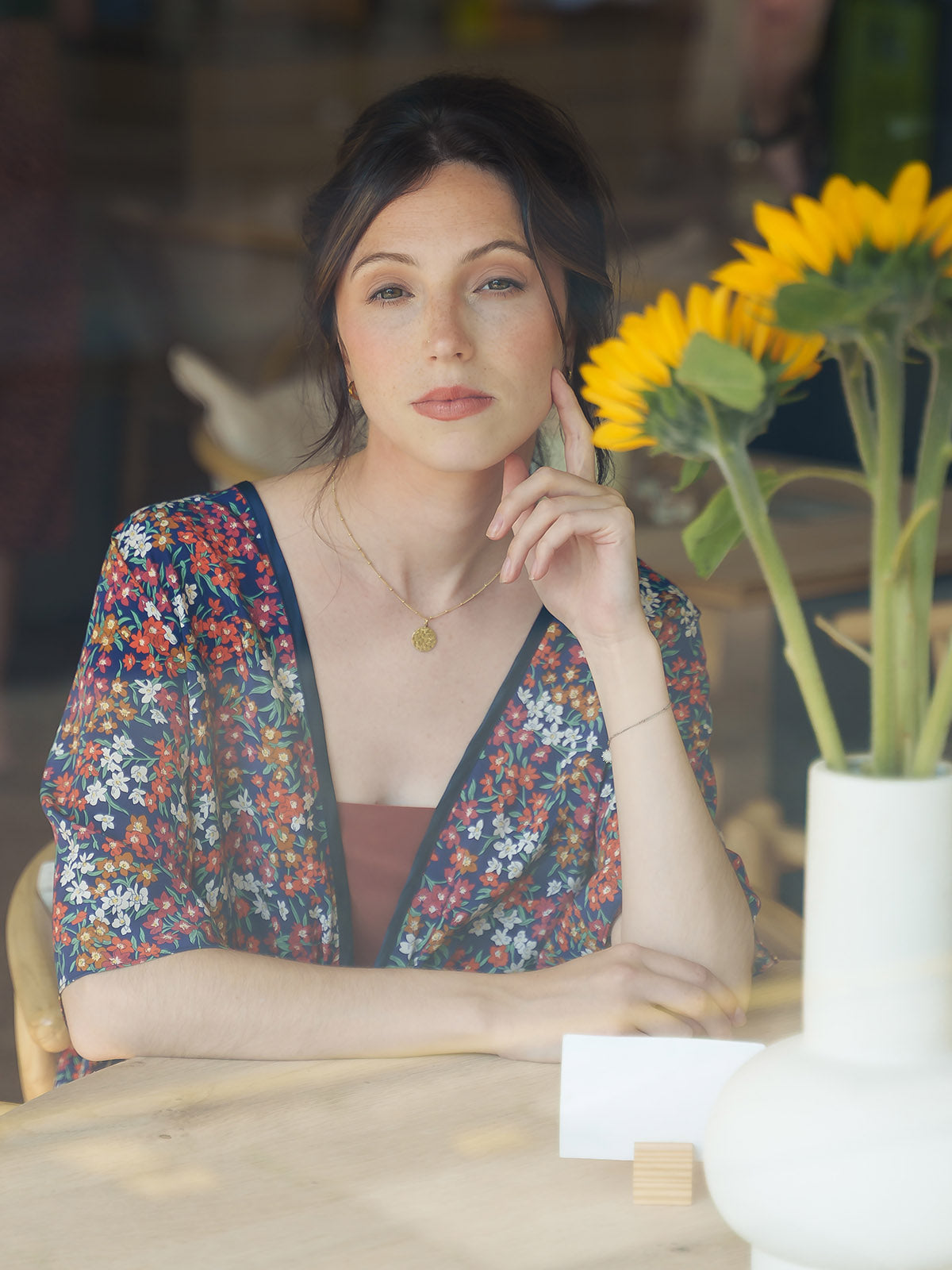 Woman in a Sea Blossom Liberty Navy Silk Bed Jacket sitting at a table with sunflowers in the background